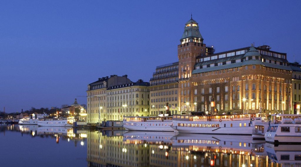 Radisson Collection Strand Hotel vid Nybroviken i Stockholm på kvällen med vatten och stadens silhuett.