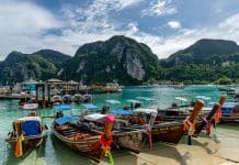 Exklusiva longtailbåtar vid turkost vatten i Phi Phi Islands med dramatiska kalkstensklippor och tropiskt landskap i bakgrunden