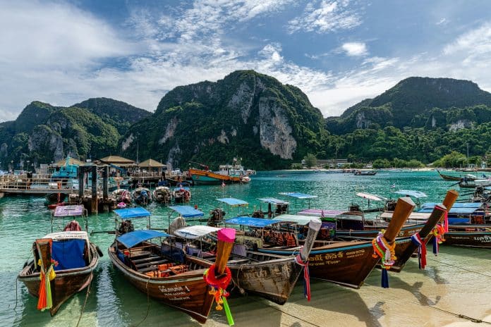 Exklusiva longtailbåtar vid turkost vatten i Phi Phi Islands med dramatiska kalkstensklippor och tropiskt landskap i bakgrunden