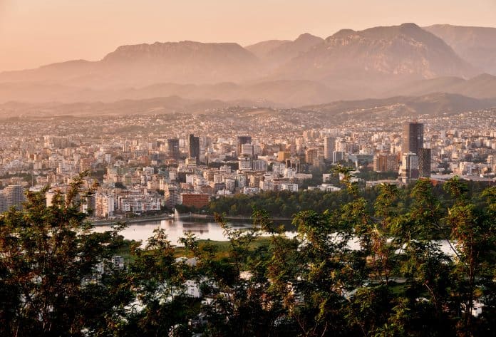 Tirana stadssilhuett i solnedgång med berg i bakgrunden och den konstgjorda sjön i förgrunden, Albanien