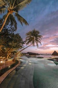 Lyxresort i Maldiverna vid solnedgång med infinitypool, palmer och överwater-villor – romantisk tropisk semester i paradis