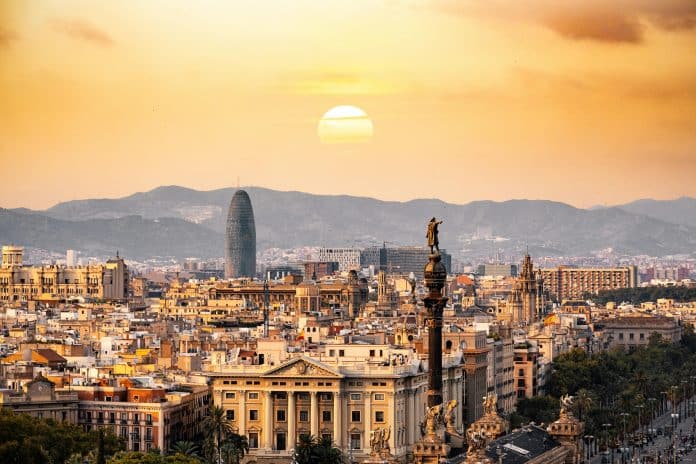 Barcelona skyline vid solnedgång med stadens historiska byggnader, Columbusmonumentet och Torre Glòries mot bergen i bakgrunden