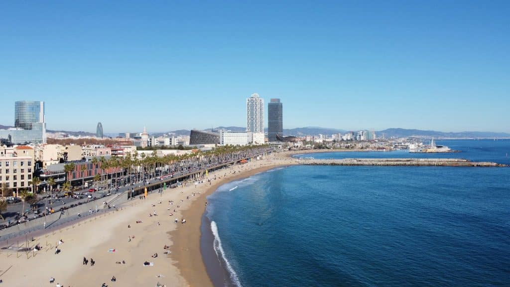 Barceloneta stranden i Barcelona med palmkantad strandpromenad, badgäster och Barcelonas skyline längs Medelhavet