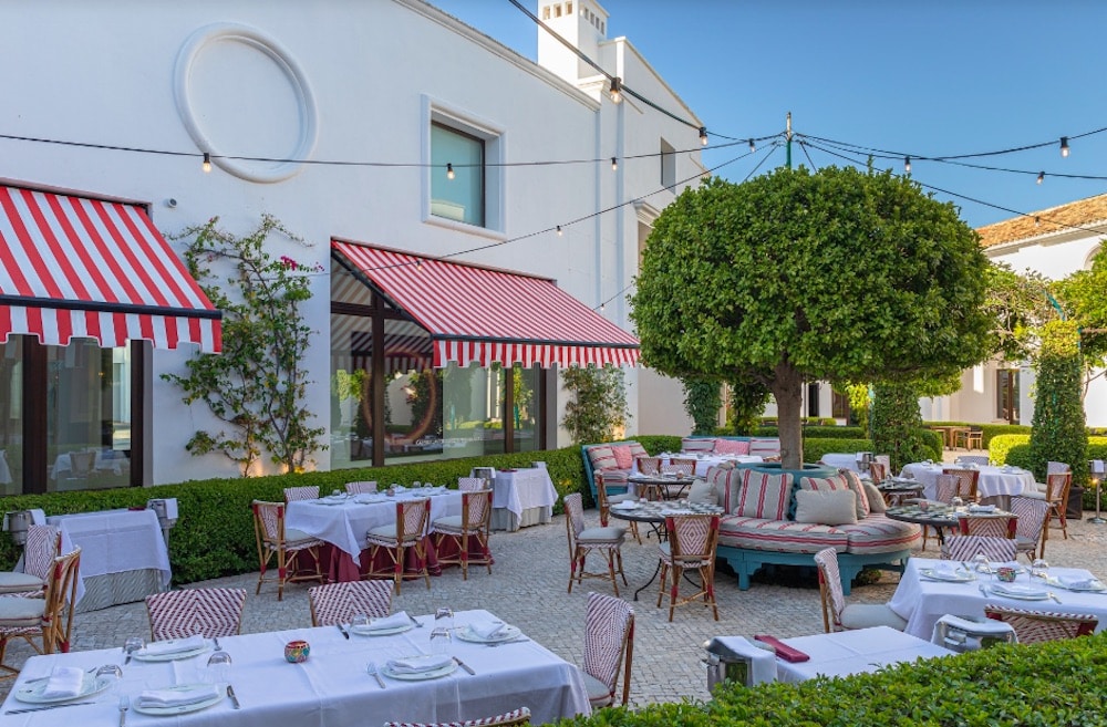 Elegant uteservering på exklusiv restaurang i Marbella med vita dukar, randiga markiser och grön innergård