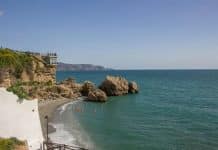 Utsikt över en pittoresk strand i Nerja på Costa del Sol i Spanien med turkost hav, klippor och badgäster under en solig dag.