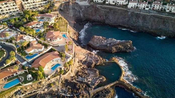 Flygfoto över exklusiva villor och naturlig havspool vid klippkusten i Los Gigantes på Teneriffa, Kanarieöarna