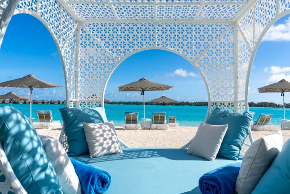 Lyxiga solstolar på vit sandstrand med parasoll och kristallklart hav på Bora Bora