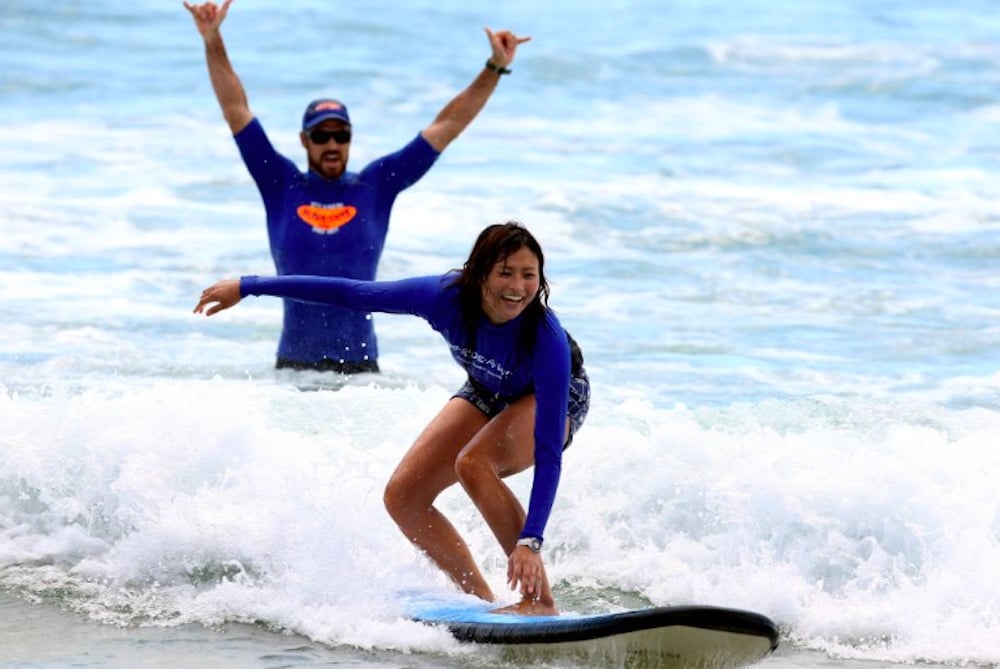 Surflektion i Australien där en nybörjare fångar sin första våg med hjälp av instruktör – en ikonisk och glädjefylld strandupplevelse.
