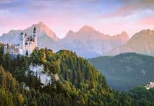 Neuschwanstein slott i Bayern omgitt av de tyske Alpene ved solnedgang, med dramatiske fjell og frodig skog i bakgrunnen