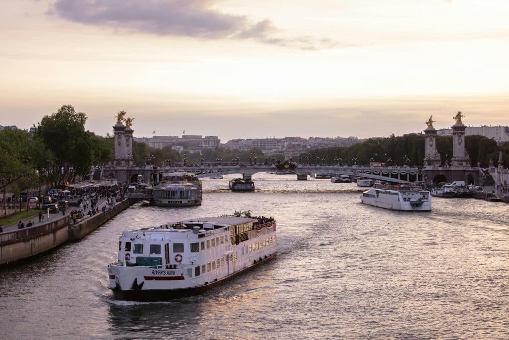 Paris vid solnedgång med sightseeingbåt på floden Seine och Pont Alexandre III i bakgrunden