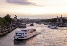 Paris vid solnedgång med sightseeingbåt på floden Seine och Pont Alexandre III i bakgrunden
