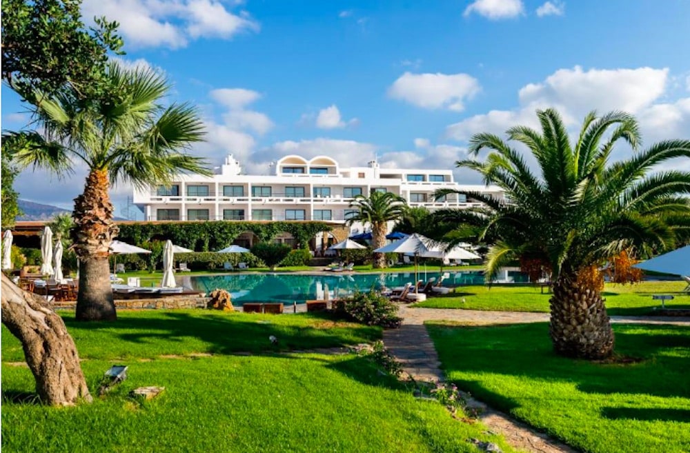 Elegant resort omgiven av palmträd och lummiga trädgårdar, med inbjudande poolområde och känsla av tidlös lyx på Kreta.