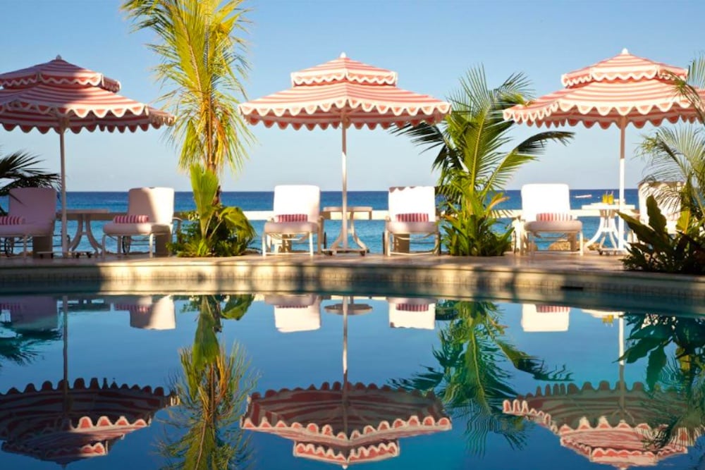 Exklusivt strandhotell på Barbados med pool, lyxiga solstolar, turkost hav och elegant resortmiljö i tropiska omgivningar.