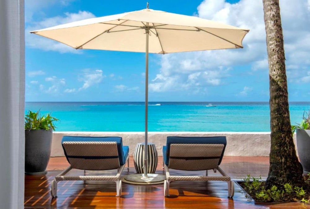 Exklusivt strandhotell på Barbados med lyxiga solstolar, turkost hav och elegant resortmiljö i tropiska omgivningar.