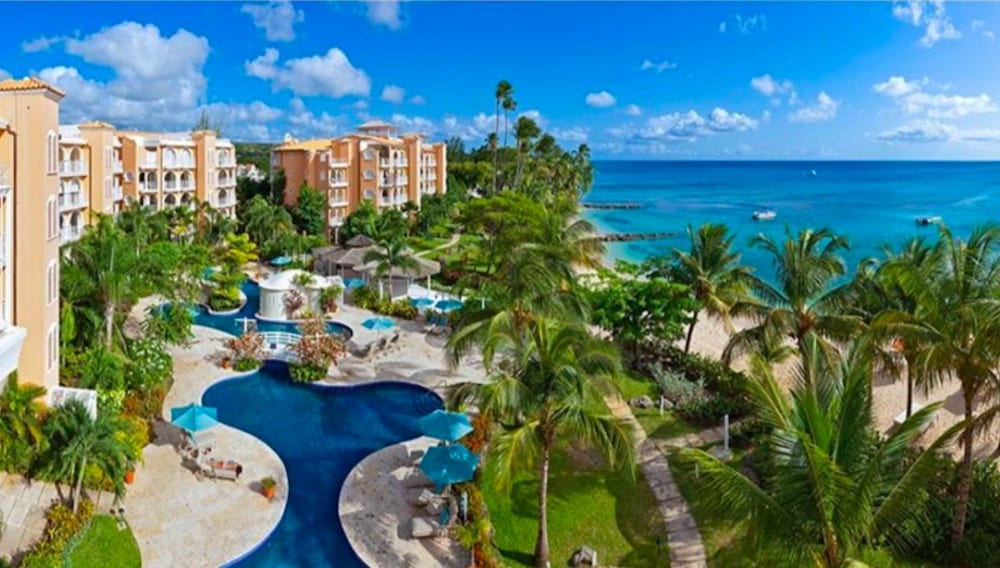 Lyxigt poolområde på Coral Reef Club omgivet av tropisk grönska, med utsikt mot havet och elegant resortmiljö.