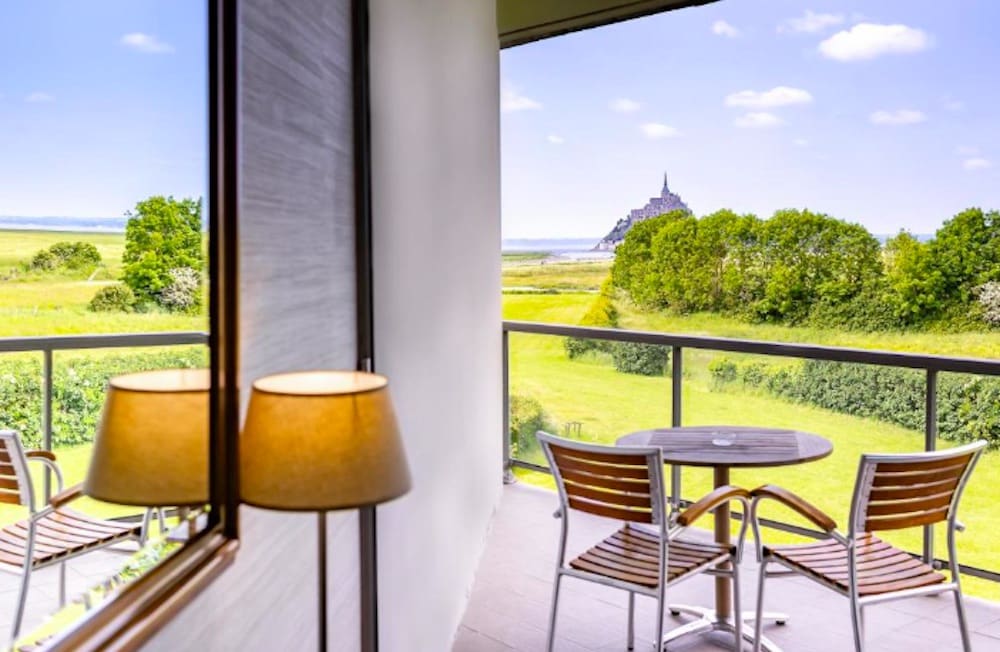 Terrass med utsikt över grönskande omgivningar och Mont-Saint-Michels historiska byggnader i bakgrunden.