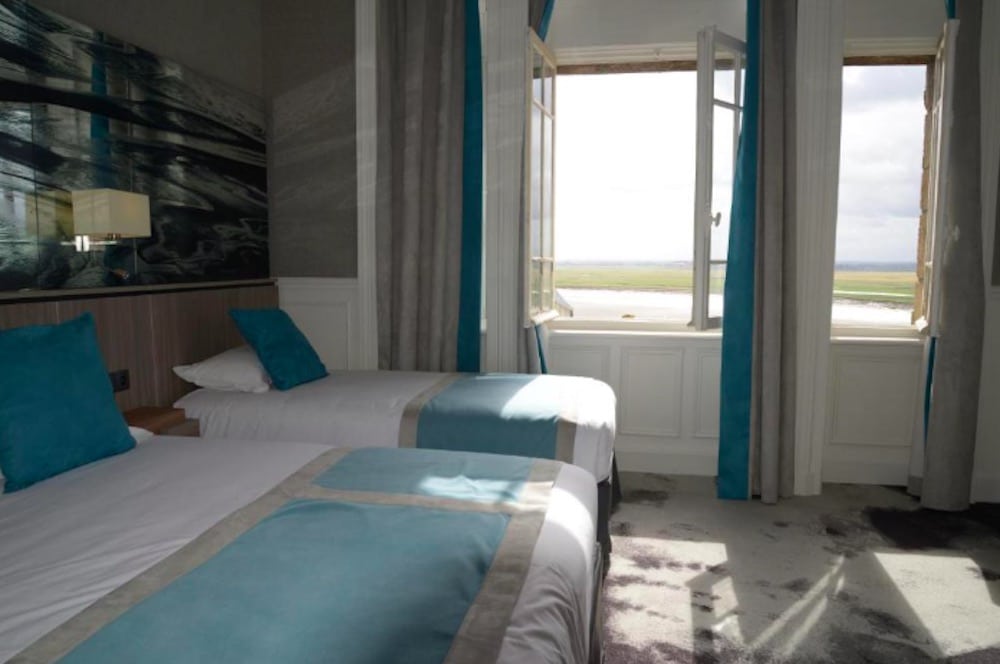Hotellrum med stilren inredning, bekväm säng och utsikt mot Mont-Saint-Michels omgivningar.