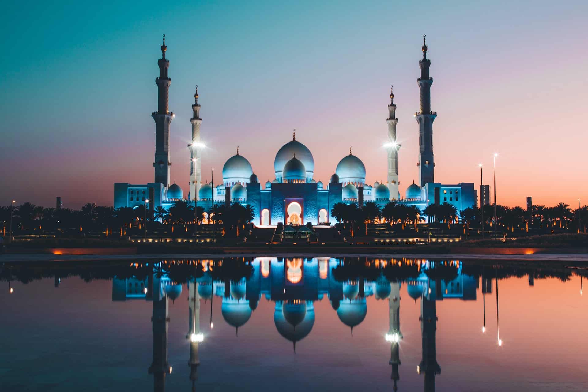 Sheikh Zayed Grand Mosque upplyst i kvällsljus, med spegelblanka vattenytor och storslagen arkitektur mot den mörknande himlen.