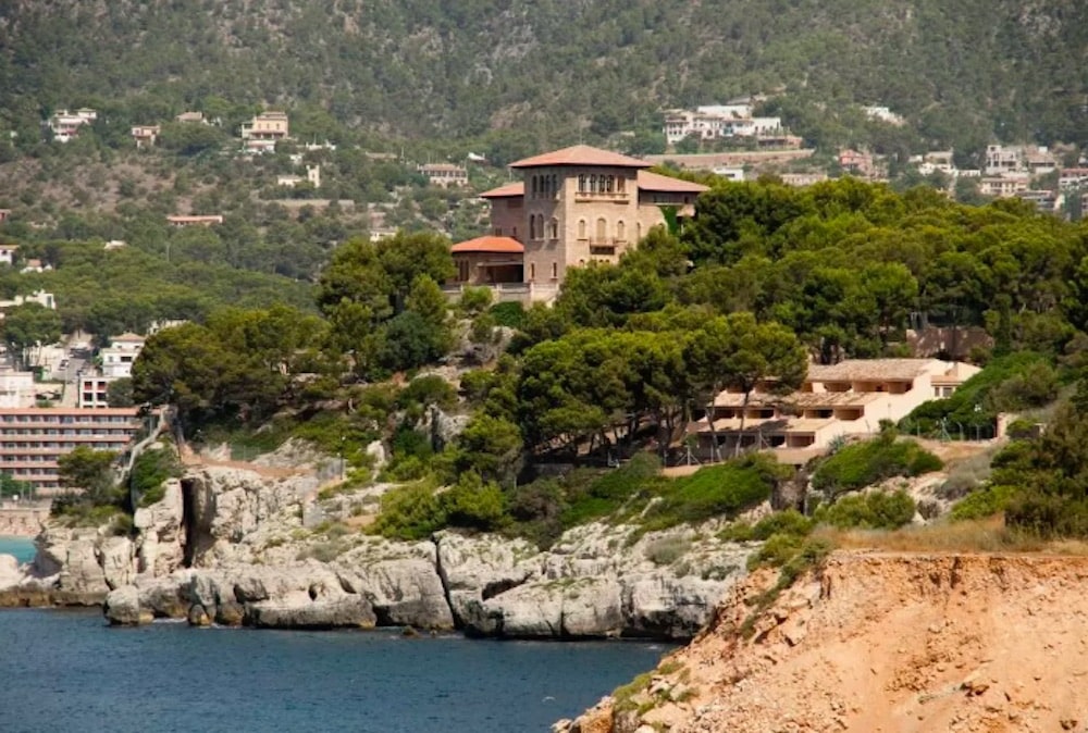 Strand och kustlinje i Cala Major med gyllene sand, klart blått hav och Palma i bakgrunden i soligt medelhavsljus.