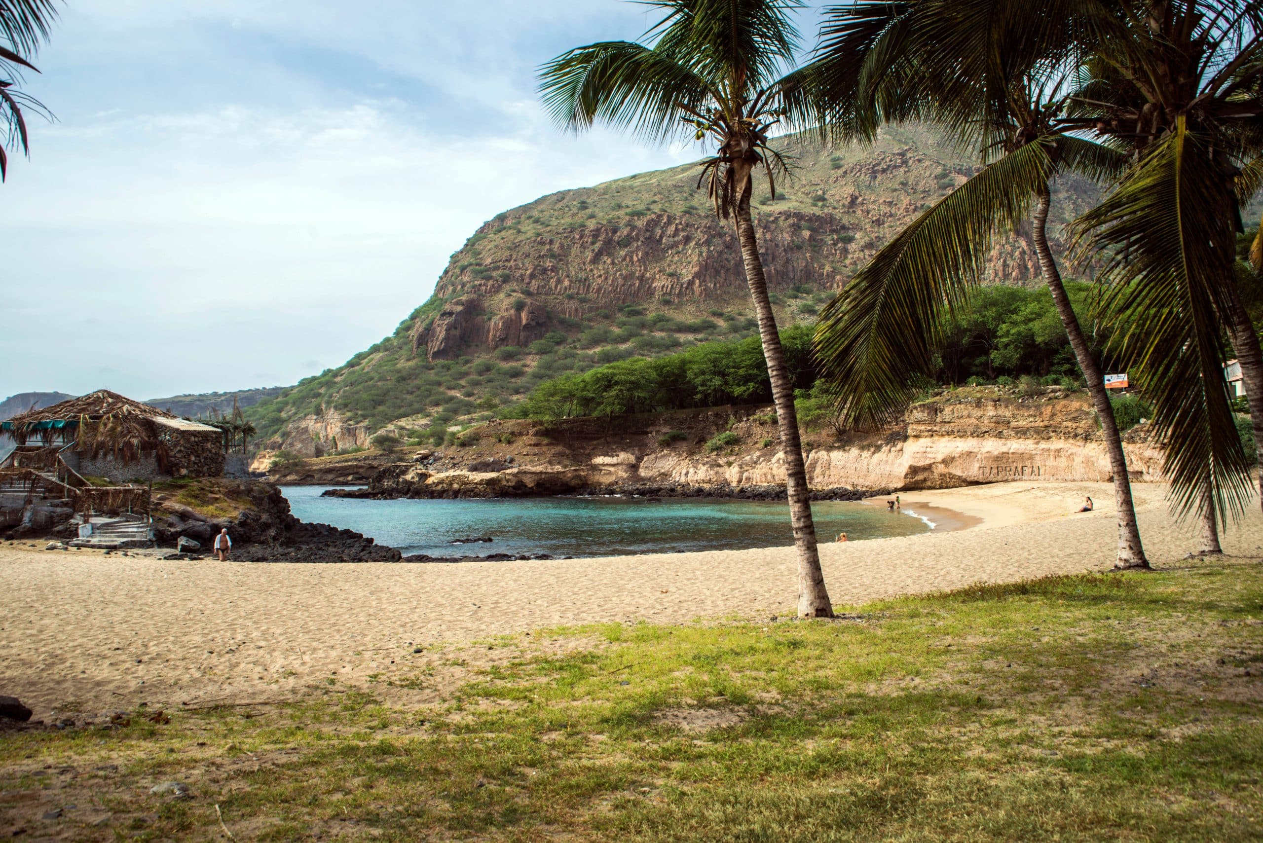 Palmkantad strand på Kap Verde, med turkost vatten, mjuk sand och dramatiska berg i bakgrunden – ett exklusivt och naturnära resmål.