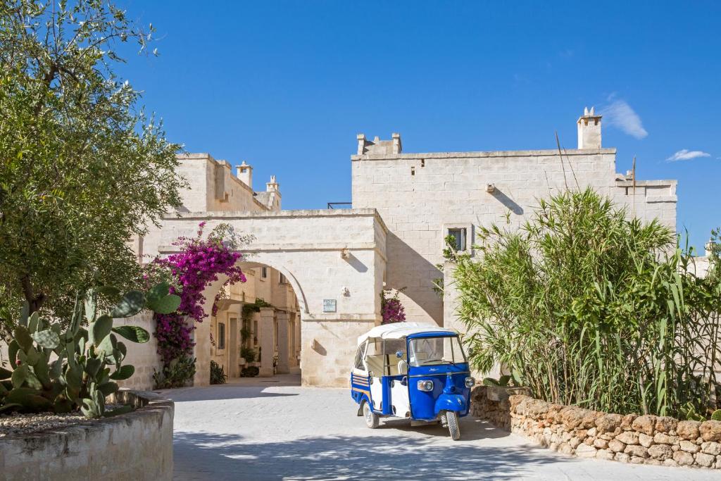 Borgo Egnazia i Italien – traditionell stenarkitektur i Puglia med vitkalkade byggnader, grönskande växter och en blå italiensk tuk-tuk vid entrén till det exklusiva lyxhotellet.