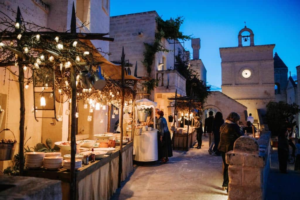 Kveldsstemning i Borgo Egnazia i Apulia, Italia, med stemningsfull utendørs servering, varme lys, historisk arkitektur og luksuriøst feriemiljø.