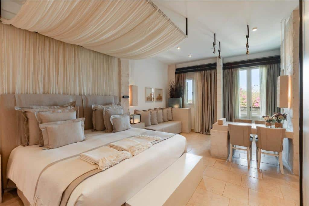 Lys og minimalistisk soverom på boutiquehotell med dobbeltseng, hvite tekstiler, steinvegger og åpent bad i naturlige, varme toner.