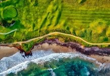 Lyxig golfbana vid havet med gröna fairways, sandstrand och turkost vatten – flygfoto över kustnära golfresort i Spanien
