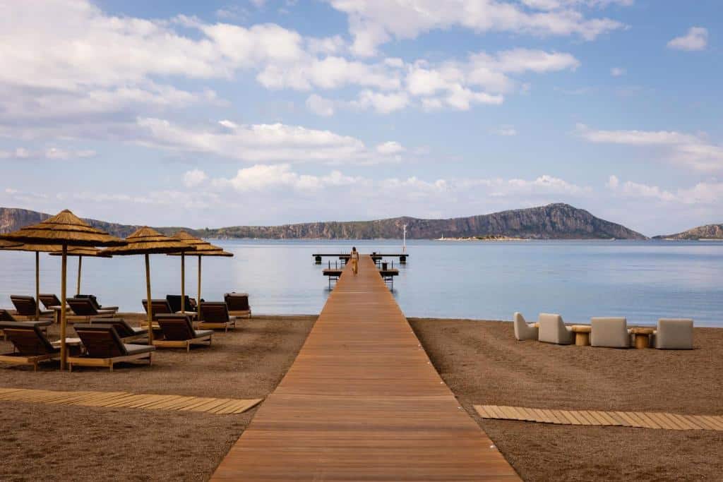 Strand och privat brygga vid W Costa Navarino i Grekland, med solstolar, parasoller och lugnt hav – en modern strandresort med exklusiv atmosfär och naturnära semesterkänsla.