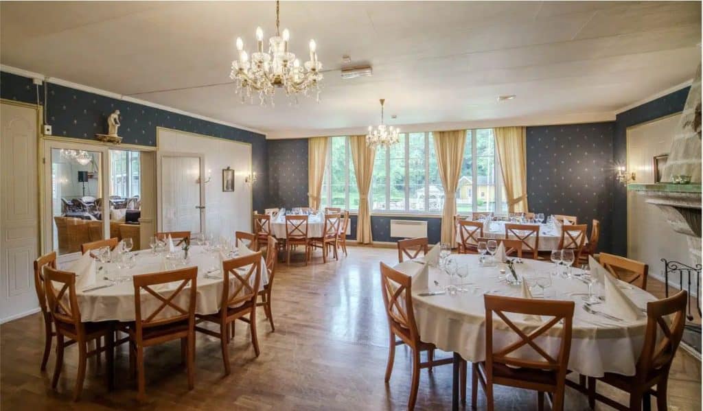 Elegant matsal på Hankø Hotell & Spa med runda bord, kristallkronor och utsikt över grönskande omgivningar