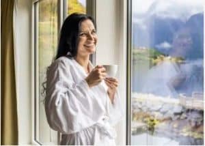 Kvinne i morgenkåpe nyter kaffe med utsikt fra hotellrom på Hankø Hotell & Spa