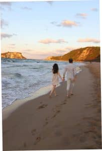 Par som promenerar hand i hand på sandstrand vid Svarta havet i Bulgarien under solnedgång
