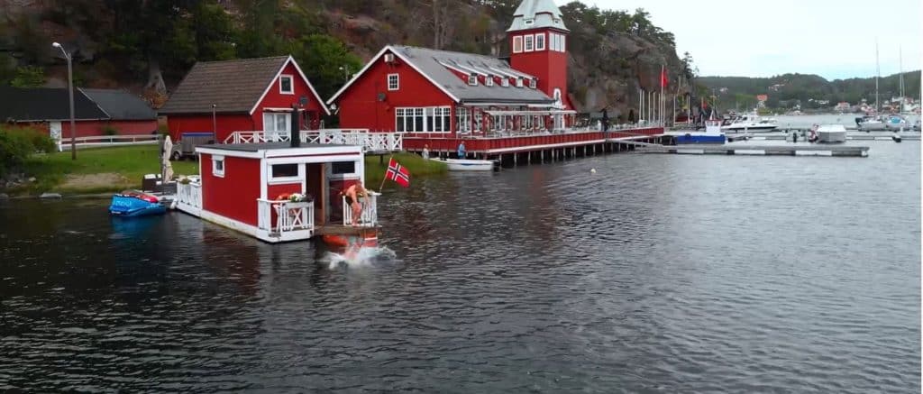Person som hoppar i havet från rött badhus vid Hankø med marina och skärgård i bakgrunden